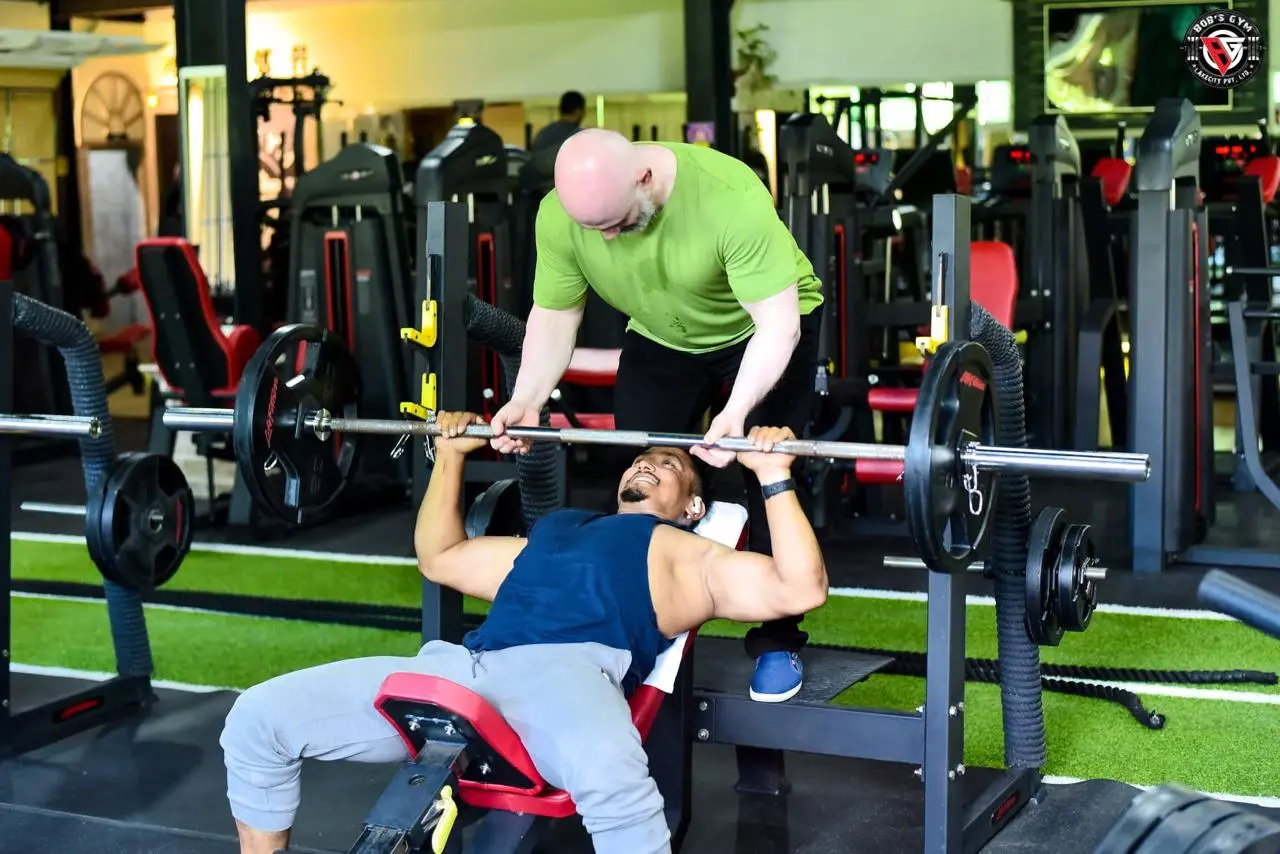 A BobsGym trainer supporting a member during a bench press